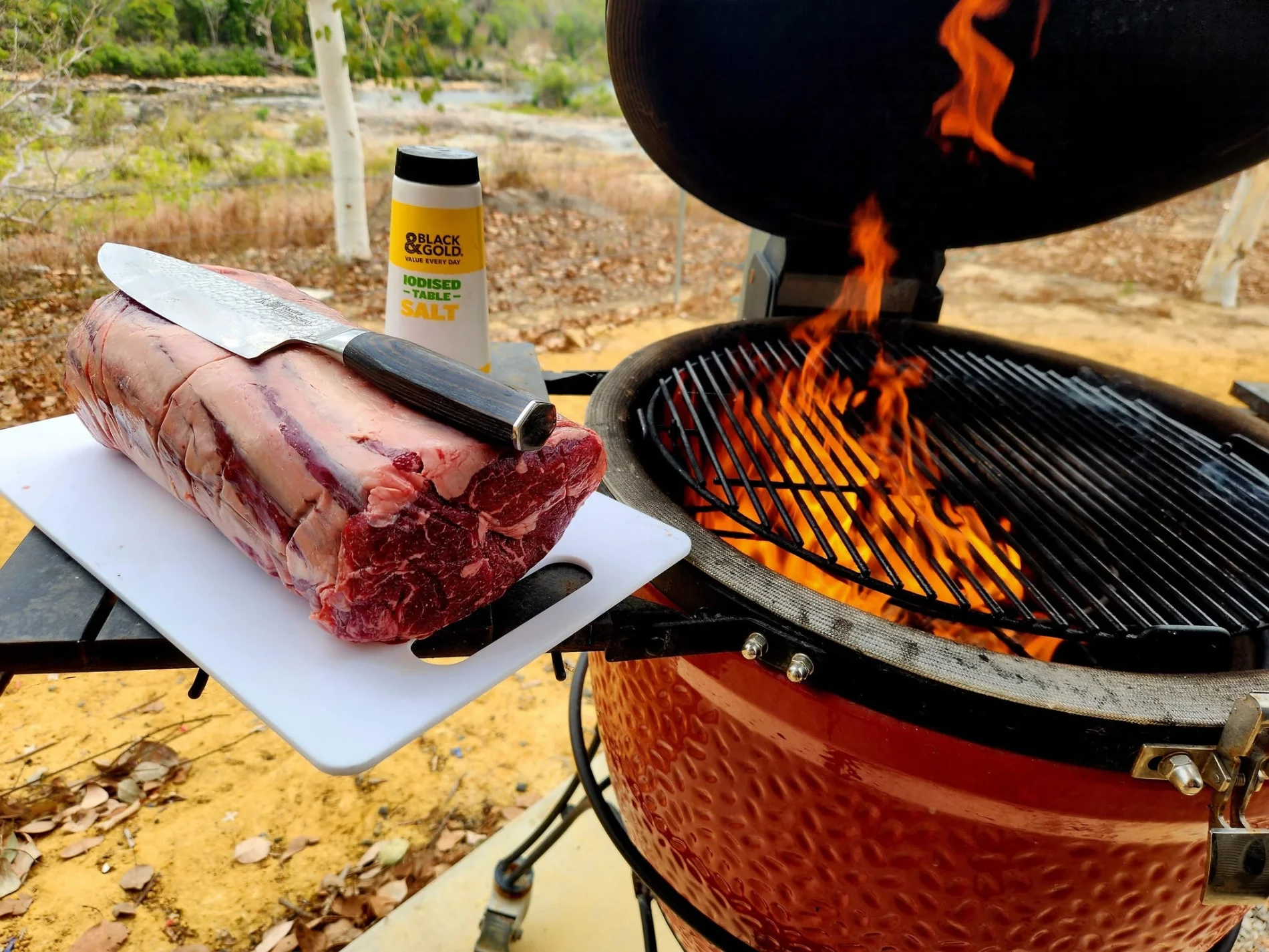 Premium beef rib on a cutting board next to a flaming grill, ready to cook from Bianchi's Butchery Cooktown